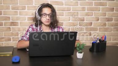 酷酷的少年男孩，一头卷曲的黑发，穿着格子衬衫，戴着耳机，跳舞，坐在笔记本电脑前